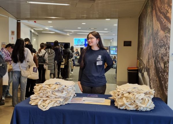 Lavanya stands behind a table at Kwong Lee Dow Building (Faculty of Education), handing out tote bags on Open Day.