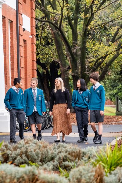 A young teacher walks with a group of students outside the school.