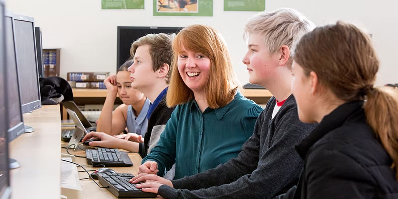 secondary students sitting at desktop computers in a classroom