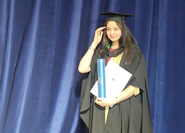 Lavanya in her cap and gown at graduation, holding her Master of Education degree.