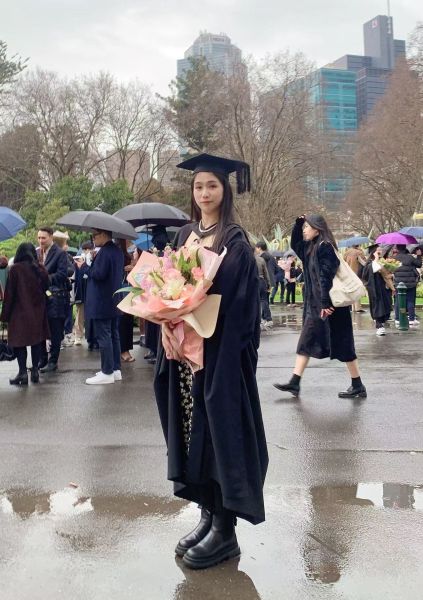 Mia at graduation dressed in her robe and hat and holding a bouquet of flowers.