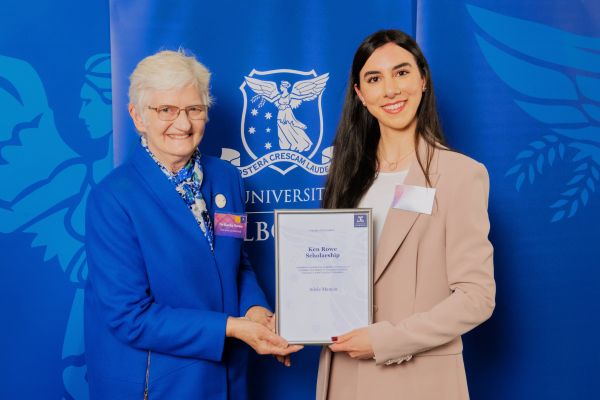An elderly woman (Dr Kathy Rowe) shakes hands with a young woman (Adele) as she hands her a certificate.
