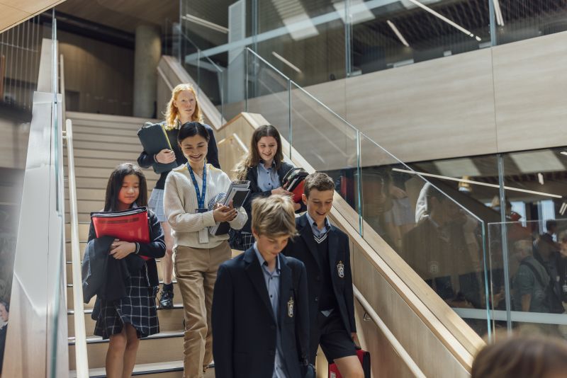 Lina descends a staircase in the middle of a group of students, smiling.